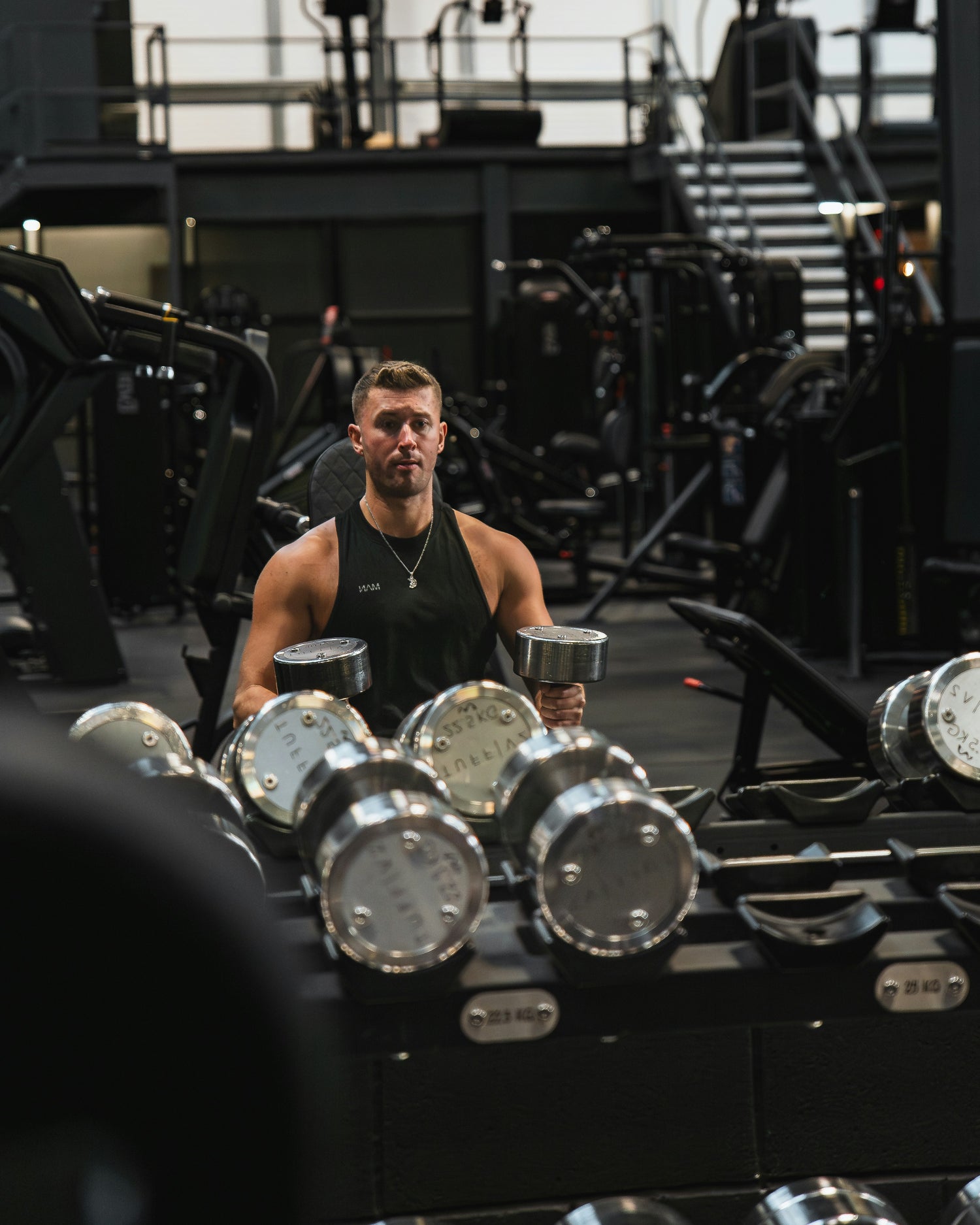 Man lifting weights in the gym, wearing a sleek silver necklace that adds style to his workout look.